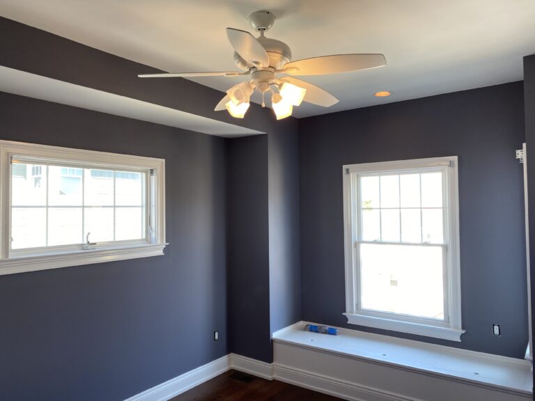 Shows the interior of a blue painted room, with nice windows and a ceiling fan above.