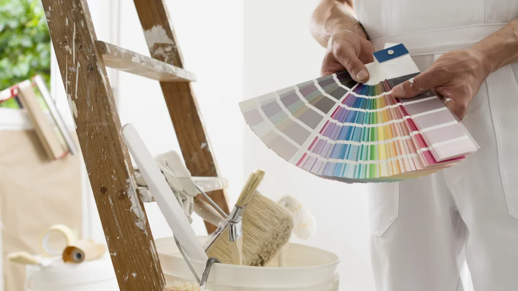 Shows a fanned-out color sample spread, next paint-stained ladder with a bucket and a brush on top.