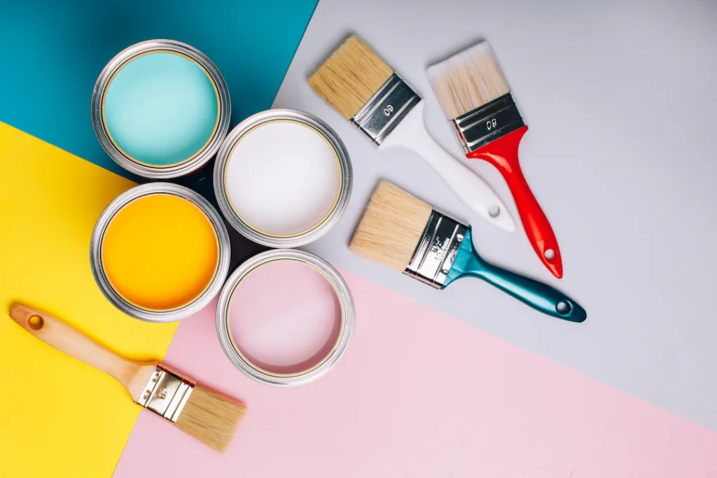 Four open cans of paint with brushes on bright background. Yellow, white, pink, turquoise colors of paint.