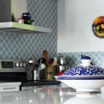 A blue container in front of a kitchen in the background with a colorful designed wall, also shows a kitchen hood, stove, and utensils.