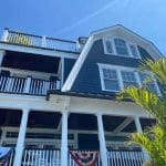 A large home, professionally painted in a deep blue and white paint with a tree in front