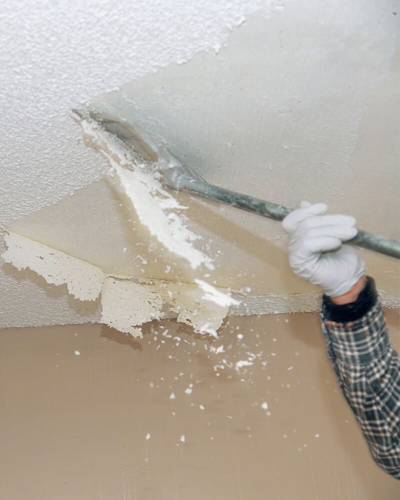 Professional popcorn ceiling removal in New Jersey with scraper tool clearing textured ceiling for a smooth finish.