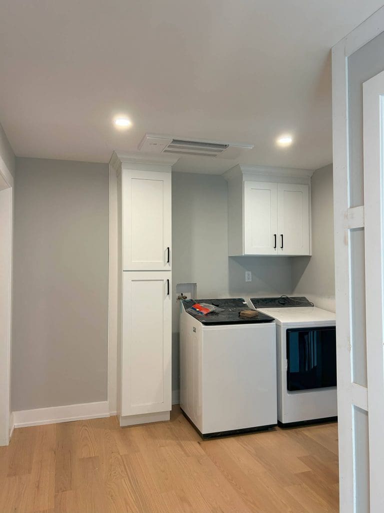 A white built-in cabinet with open shelves and closed doors, featuring a ladder and tools during assembly or installation.