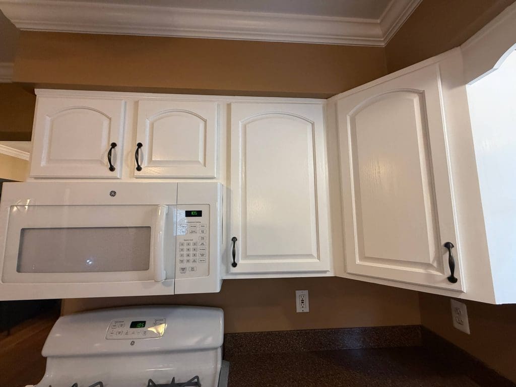 A kitchen with white cabinets, a built-in microwave, and a gas stove below, featuring brown walls and a granite countertop with electrical outlets.