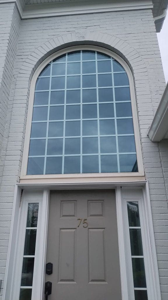 Arched window above front door of a painted brick home in New Jersey, featuring light gray trim
