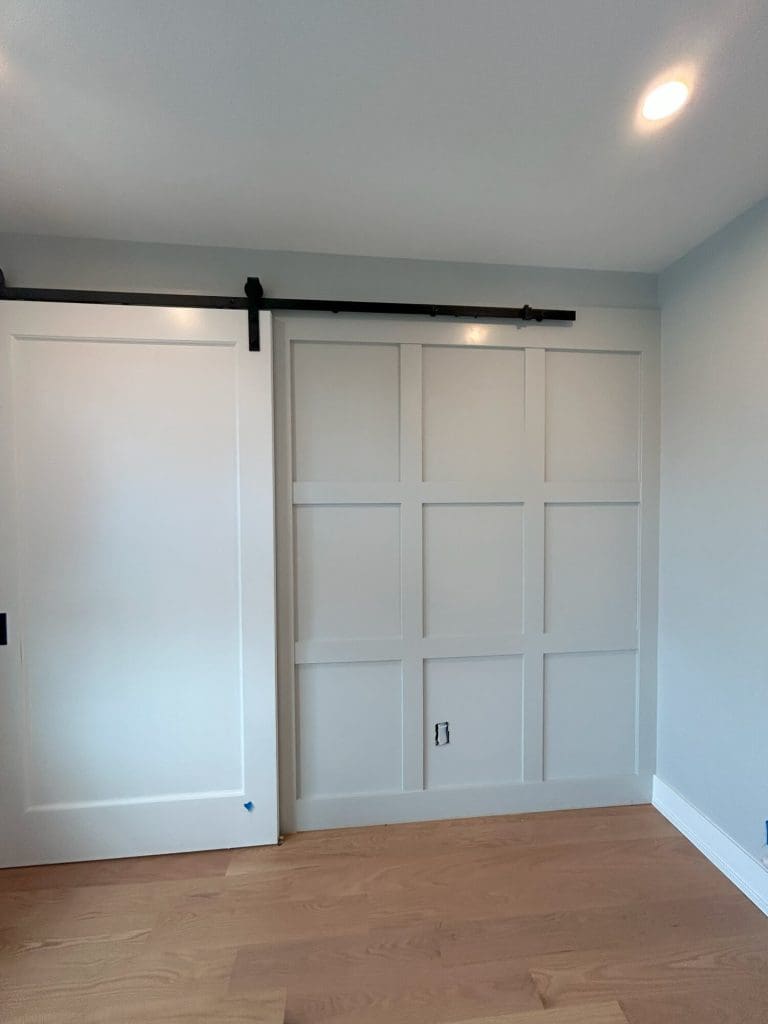 Modern bedroom with wood floors, white sliding barn door, and accent wall paneling in New Jersey home.