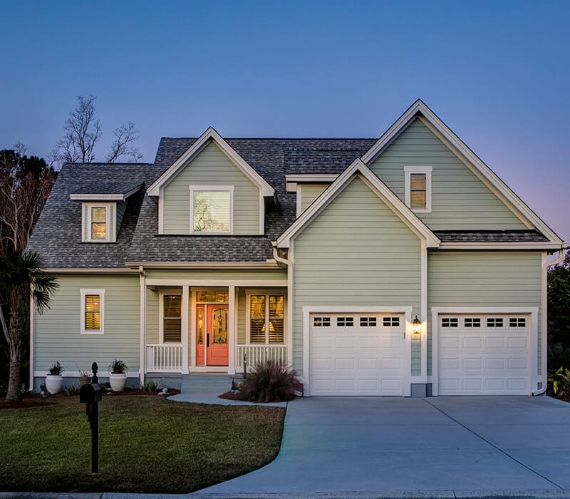 services-exterior-painting-asbury-nj Two-story suburban home with gray siding, white trim, and double garage at dusk in New Jersey