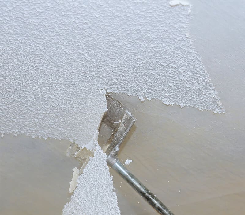 services-popcorn-ceiling-removal-asbury-nj Close-up of popcorn ceiling removal in progress with a scraping tool in Ocean County, NJ