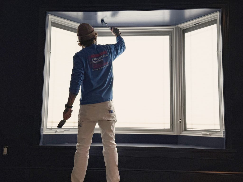 Carfagno painter rolling dark paint above a bay window.