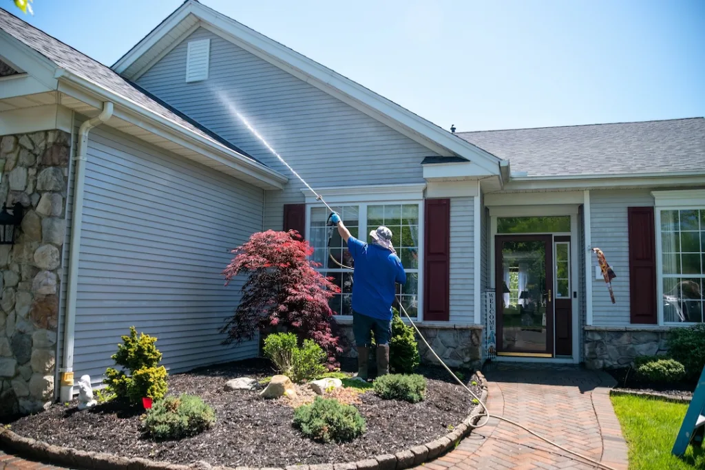 Professional pressure washing gray vinyl siding on a home.
