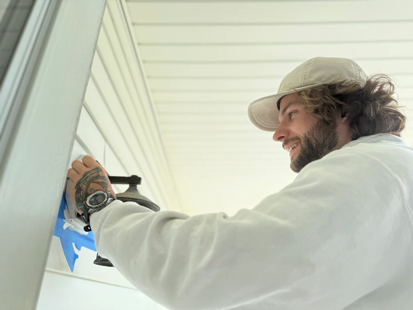 Painter brushing white exterior trim beside a masked wall-mounted light fixture.