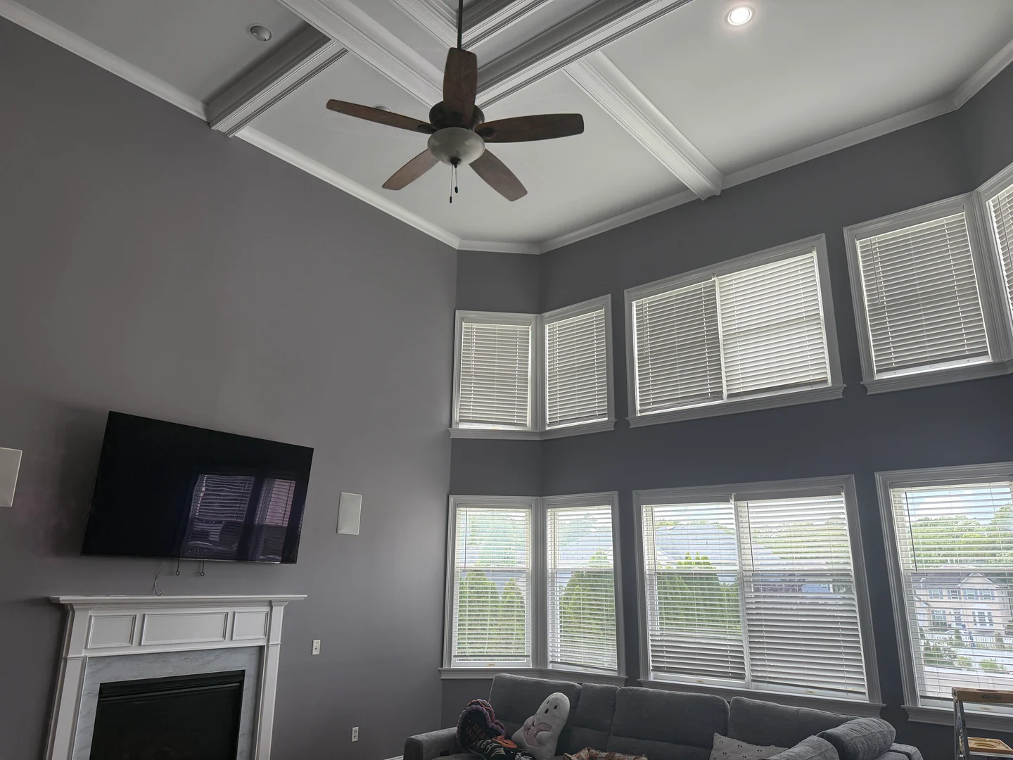 Tall gray living room with a white coffered ceiling, fireplace trim, and two levels of windows.
