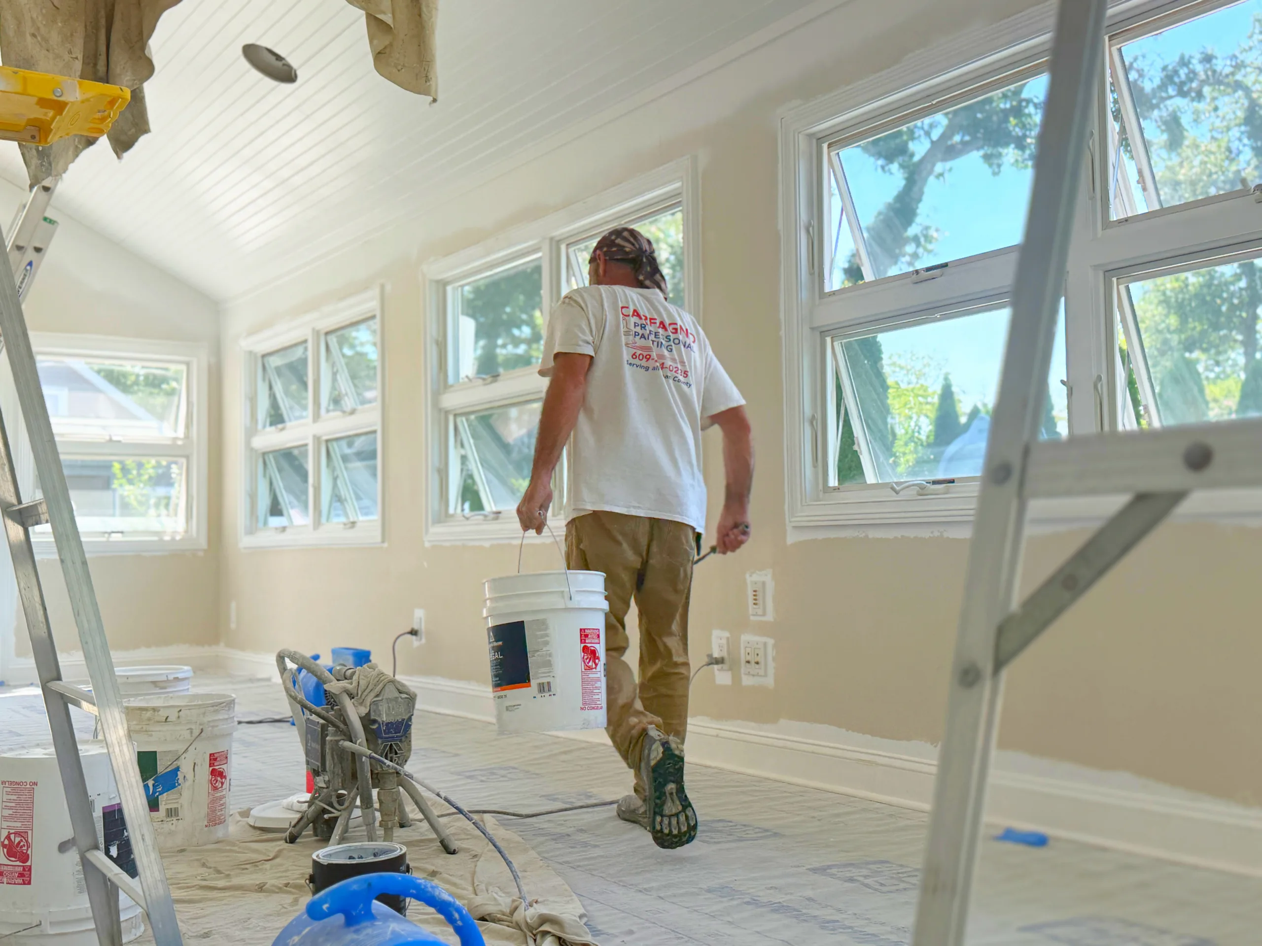 Carfagno painter carrying supplies through a protected sunroom during an interior painting project